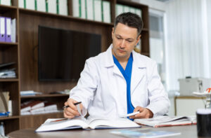 Doctor Reviewing Patient Records In A Modern Office Setting. A Healthcare Professional Is Focused On Reviewing Patient Records At His Desk - Contabilidade em Brasília